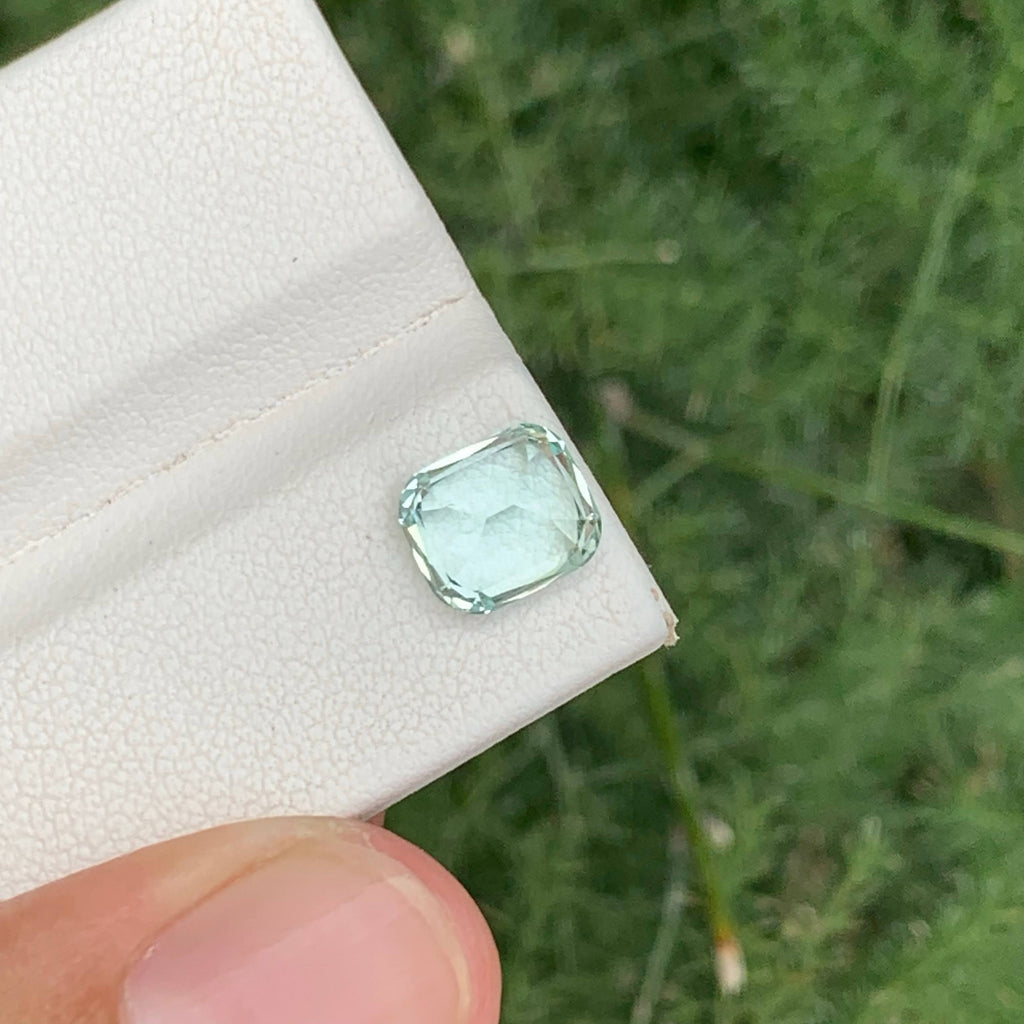 Green gemstone held on a white cloth against a green outdoor background