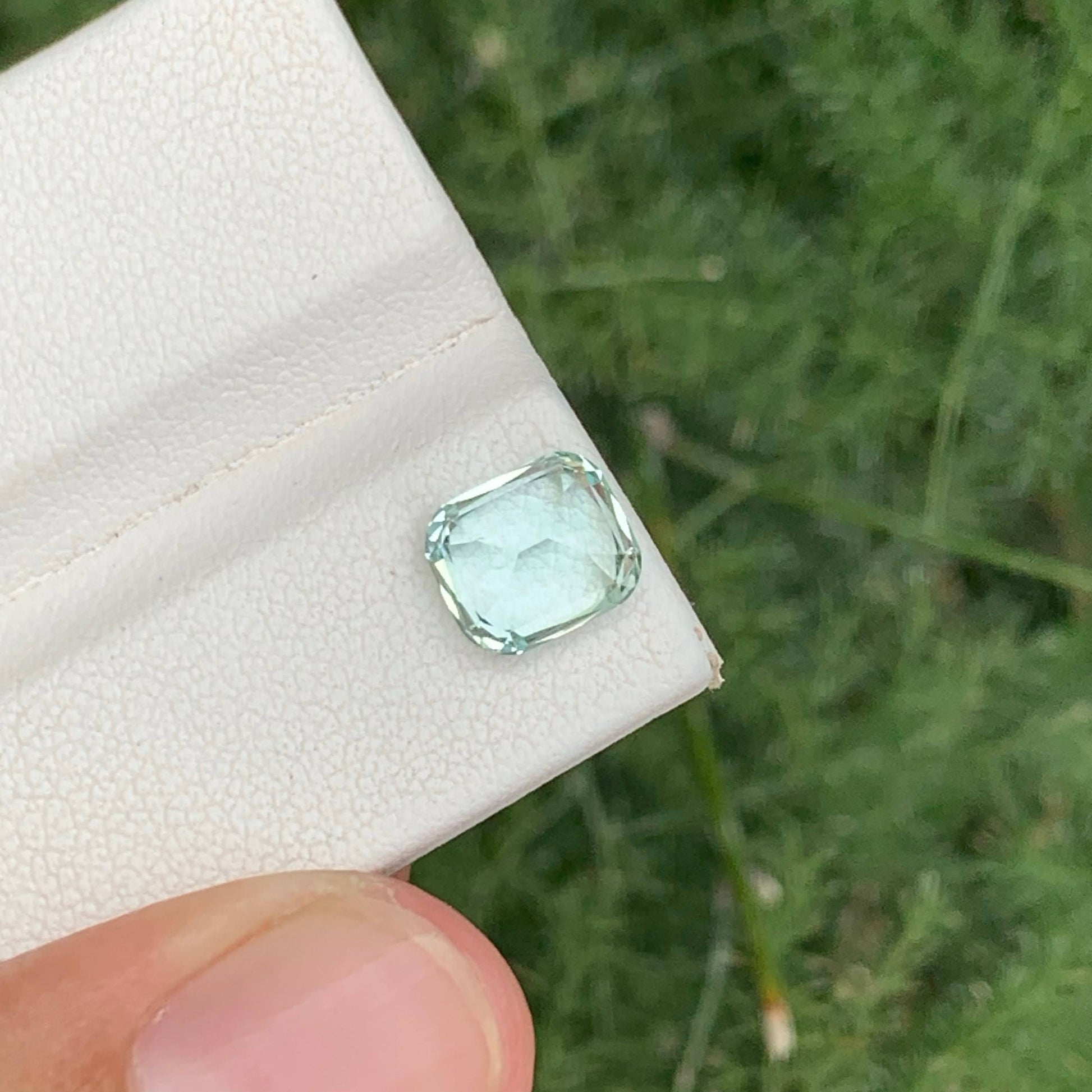 Green gemstone held on a white cloth against a green outdoor background