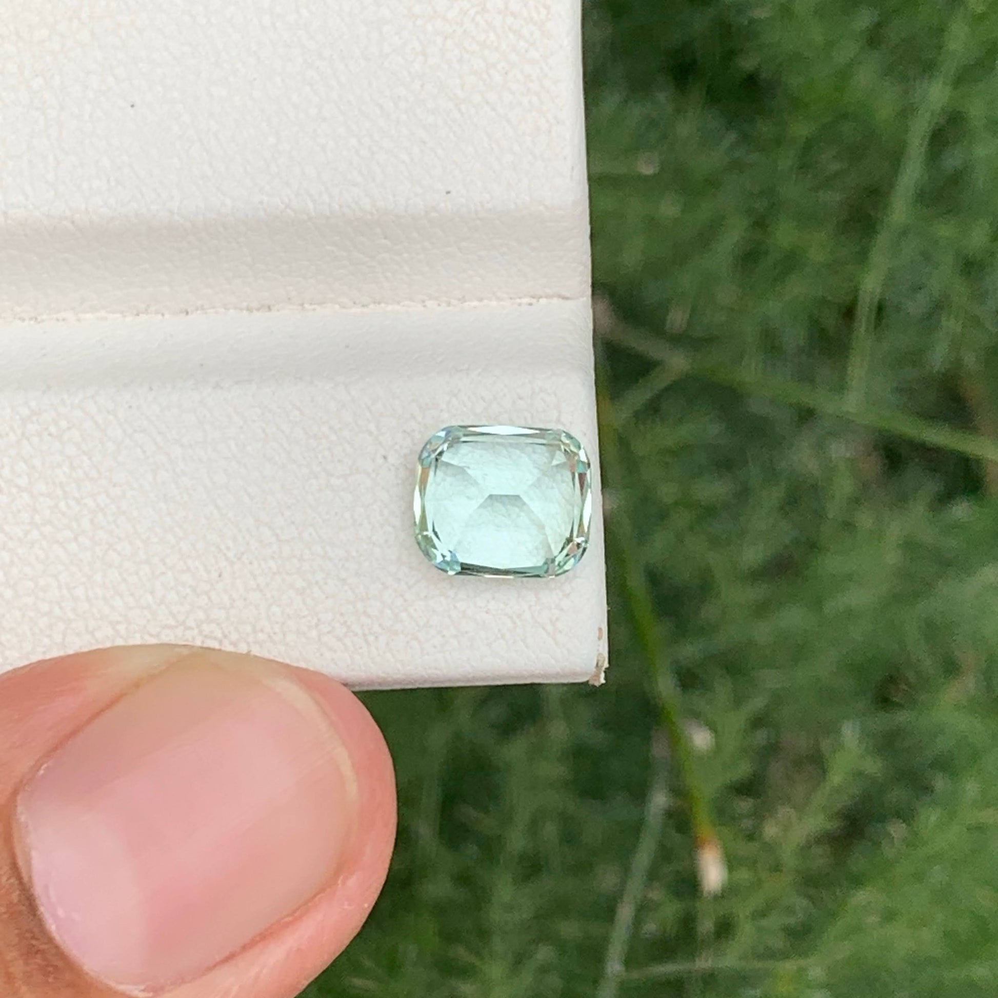Green gemstone held between fingers against a natural background
