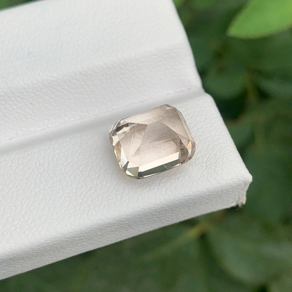 Faceted gemstone on a white surface with a blurred green background