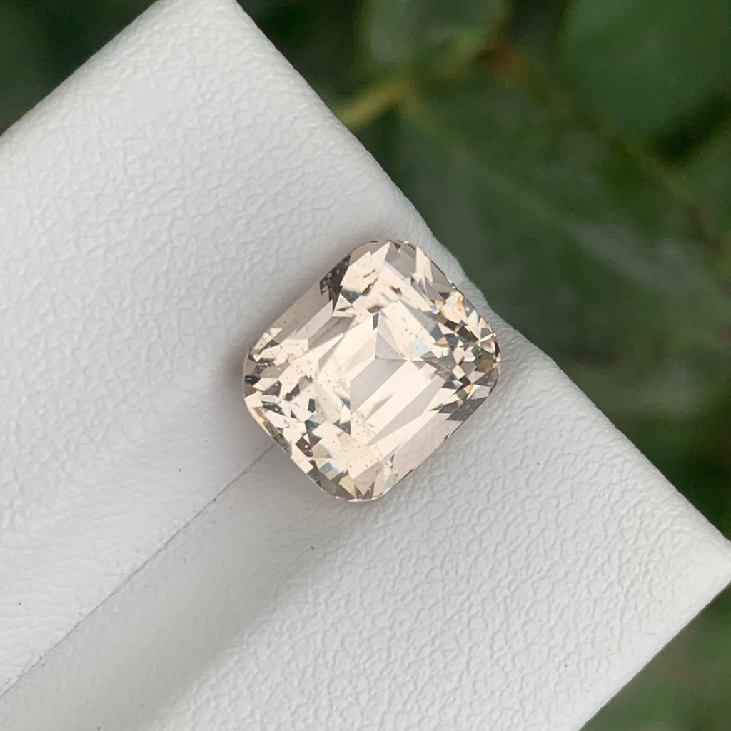 5.80 Carats Quality Peach Topaz Stone Cushion Cut Natural Pakistani Gemstone on a white stand with green leaves in the background