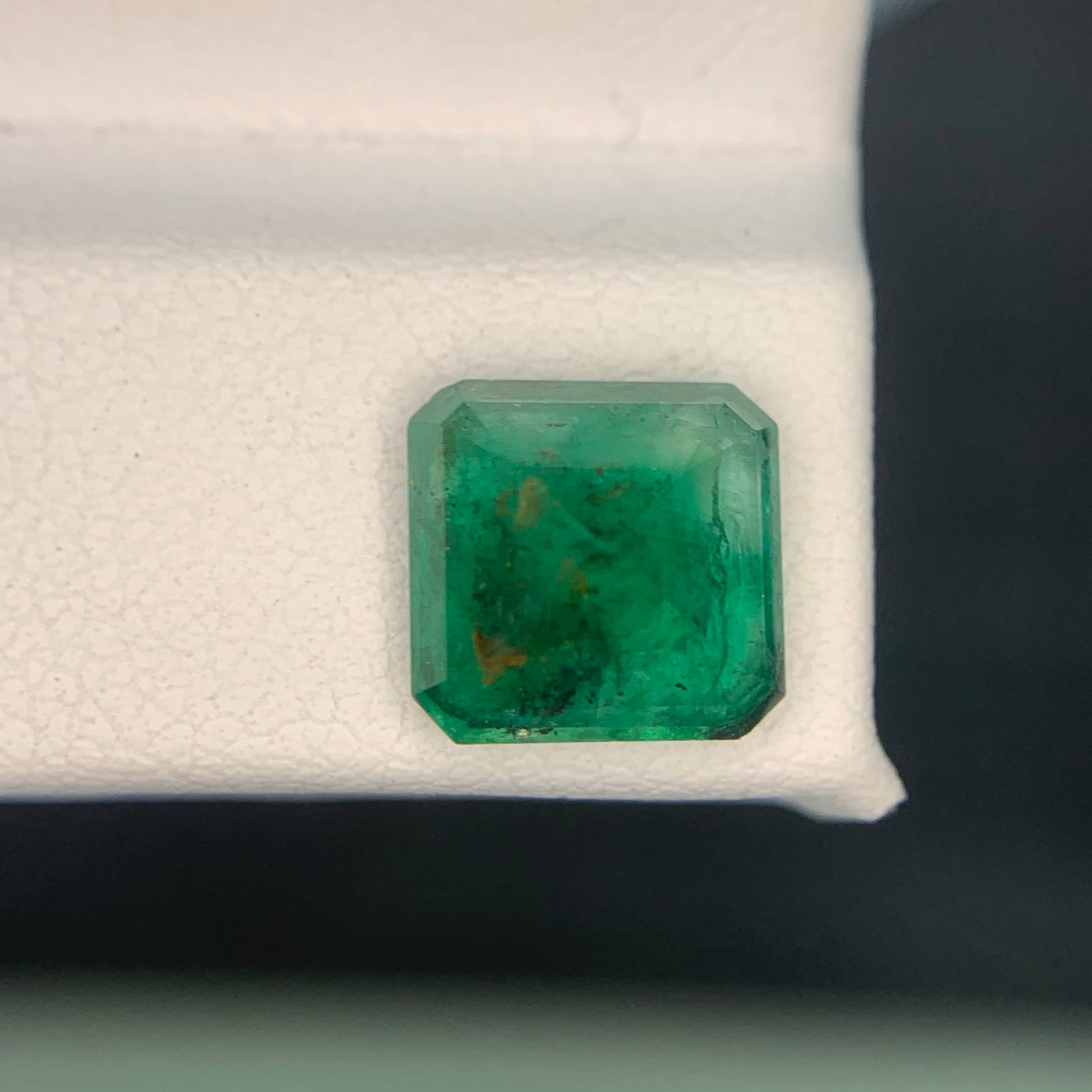 Emerald gemstone on a white cushion against a dark background