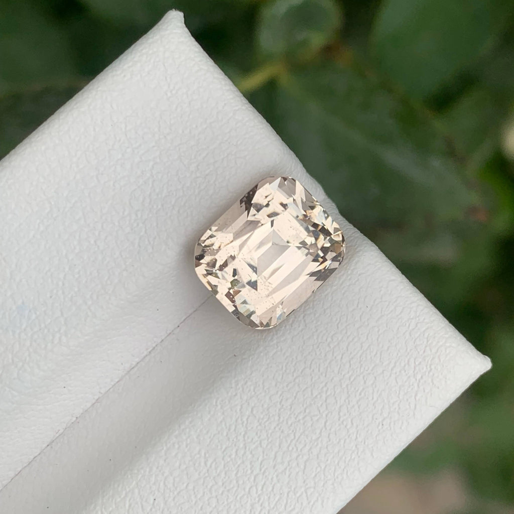 5.80 Carats Quality Peach Topaz Stone Cushion Cut Natural Pakistani Gemstone on a white stand with green leaves in the background