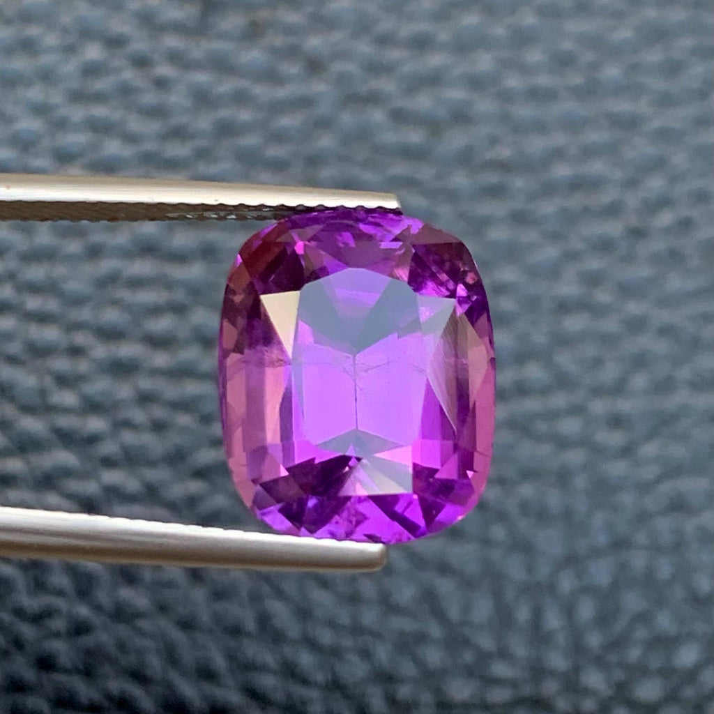 10.75 Carat Purple Amethyst Purple gemstone held by tweezers against a textured gray background