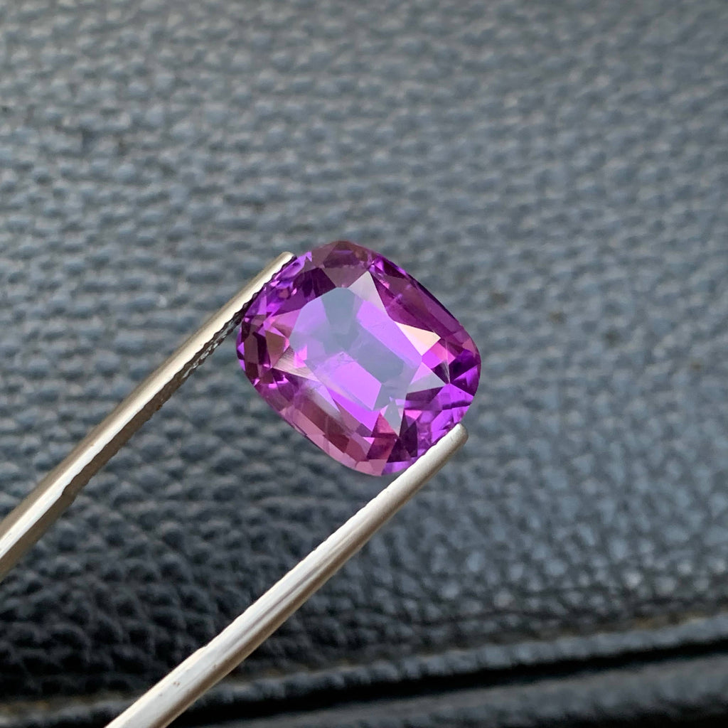10.75 Carat Purple Amethyst Purple gemstone held by tweezers against a textured gray background