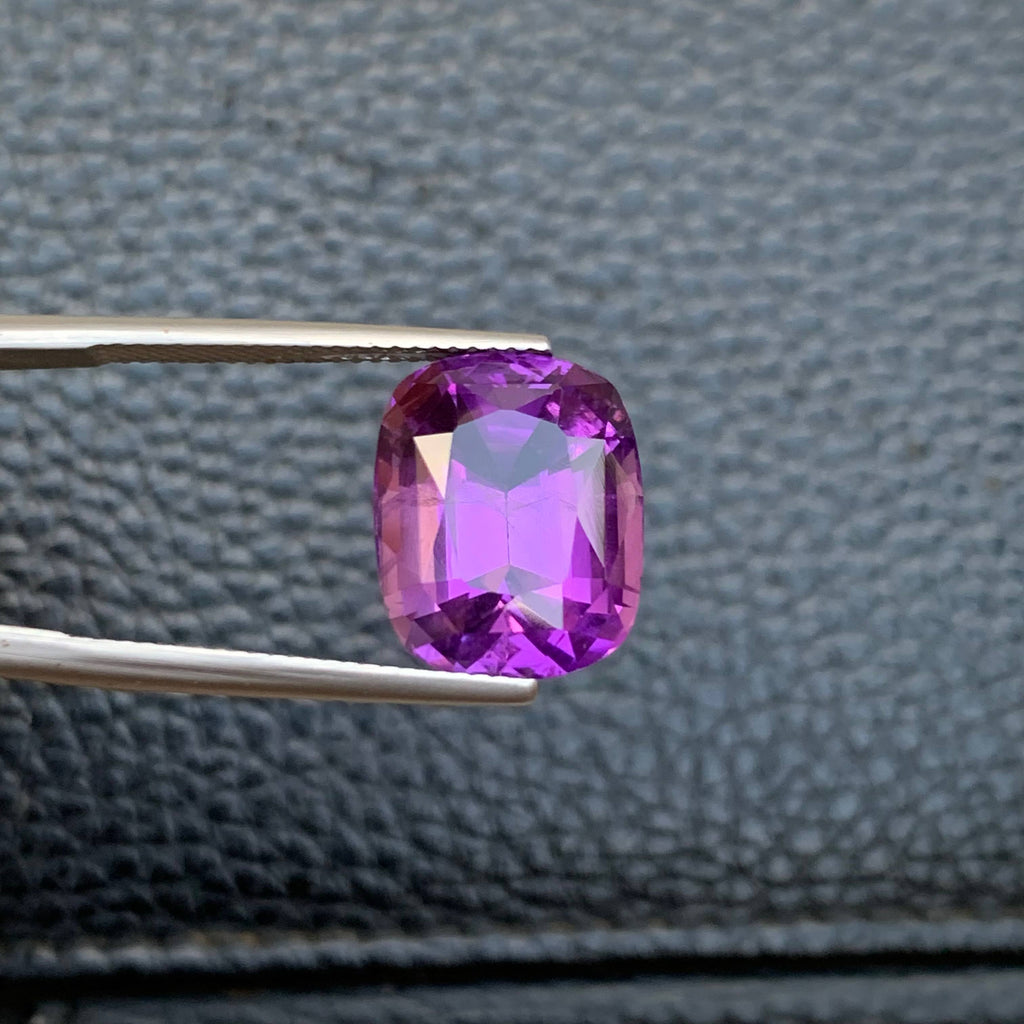 10.75 Carat Purple Amethyst Purple gemstone held by tweezers against a textured gray background