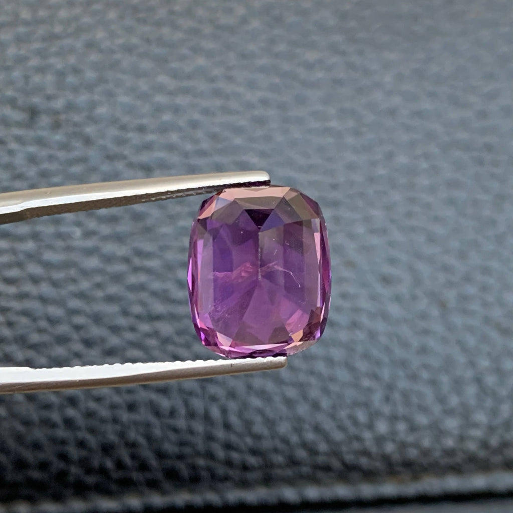 10.75 Carat Purple Amethyst Purple gemstone held by tweezers against a textured gray background
