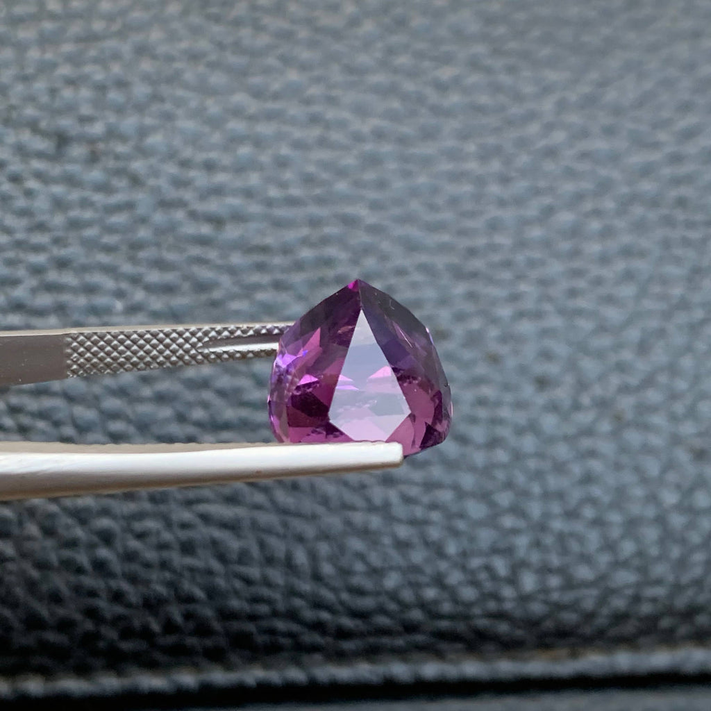 10.75 Carat Purple Amethyst Purple gemstone held by tweezers against a textured gray background