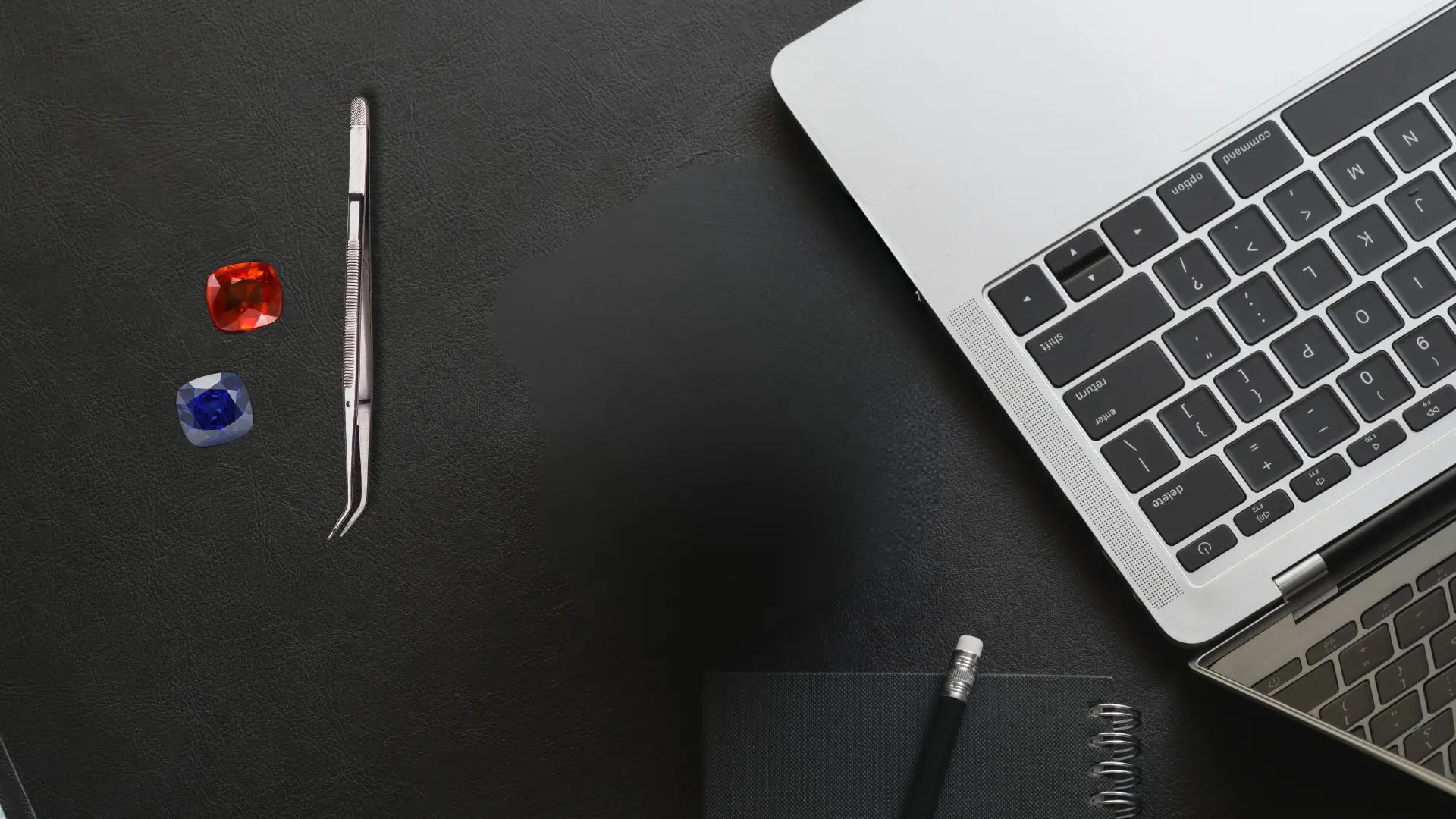 Laptop on a dark surface with tweezers, gemstones, and a notebook used as background Image