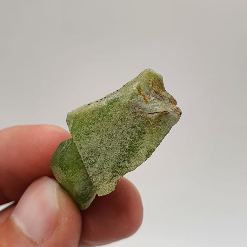 Hand holding a green crystal against a plain background at Gandhara Fine Minerals 